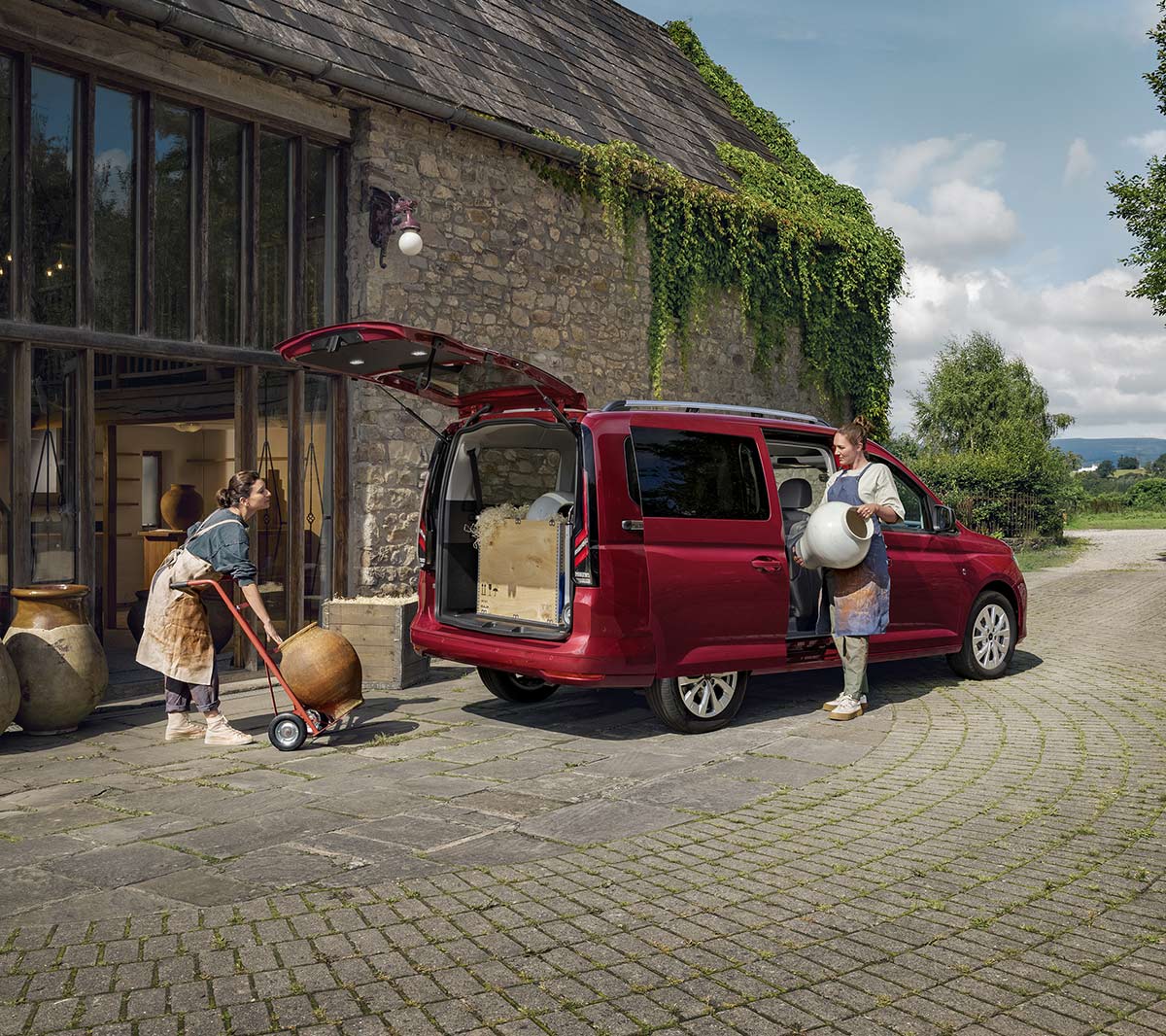 Ford Tourneo Connect in Rot. Heckansicht, parkt mit geöffnetem Kofferraum vor einem Haus.