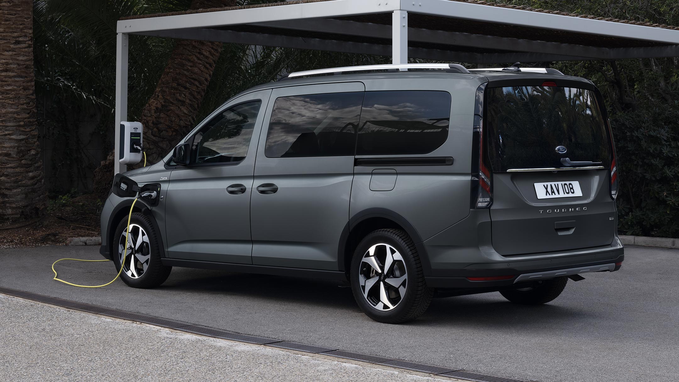 Ford Tourneo Connect in Grau. Dreiviertelansicht, angeschlossen an einer Ladestation.