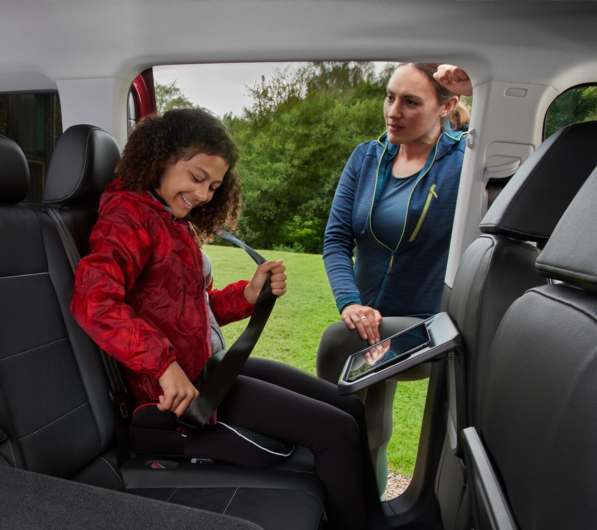 Ford Tourneo Connect Innenraum. Ansicht der 2. und 3. Sitzreihe, Mädchen schnallt sich an