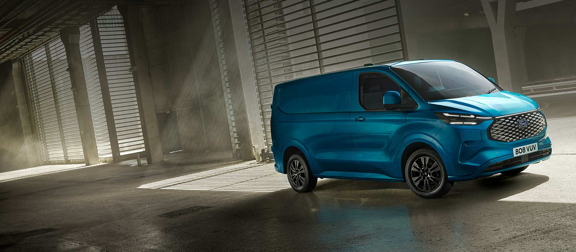 Ford E-Transit Custom Kastenwagen Einzelkabine in Blau. Dreiviertelansicht, stehend in einer Lagerhalle.
