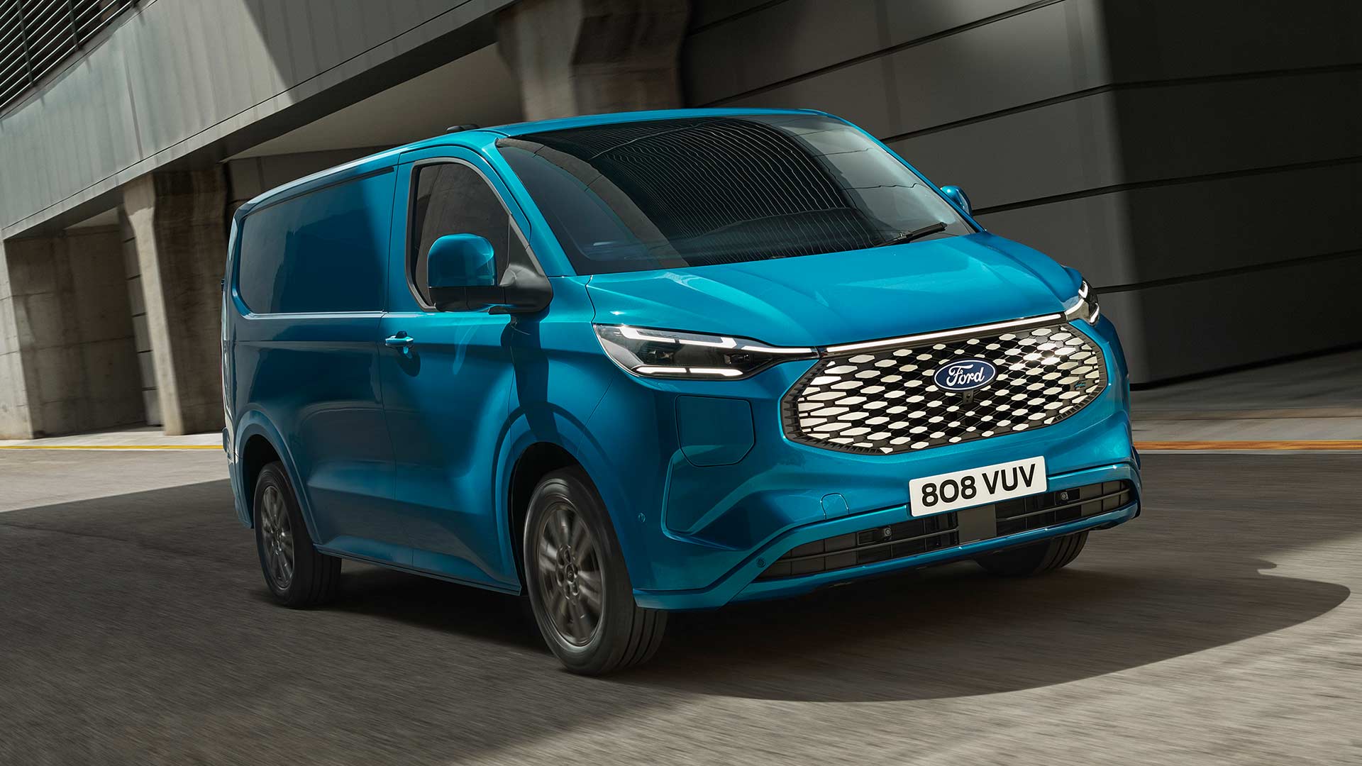 Ford E-Transit Custom in Blau. Dreiviertelansicht, fährt eine Straße entlang.