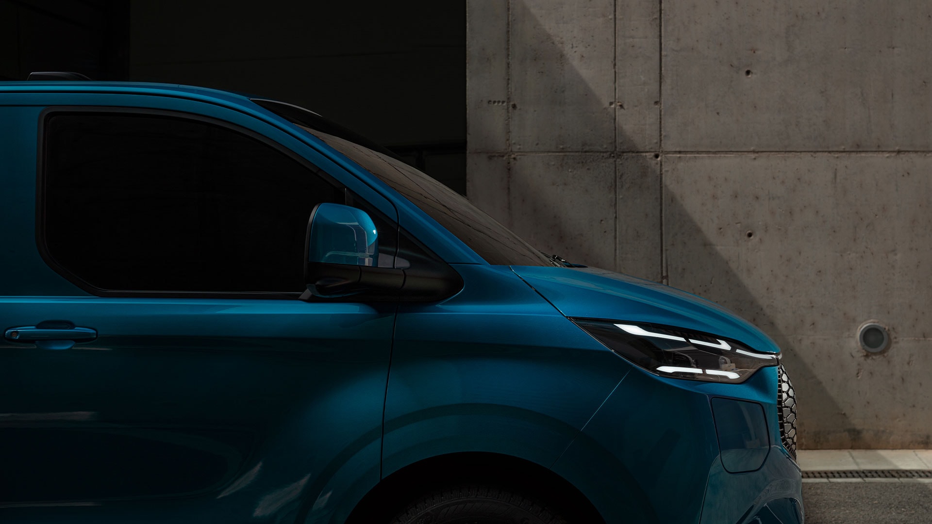 Ford E-Transit Custom in Blau. Seitliche Ansicht des Fahrzeugs mit Fokus auf die LED-Scheinwerfer.
