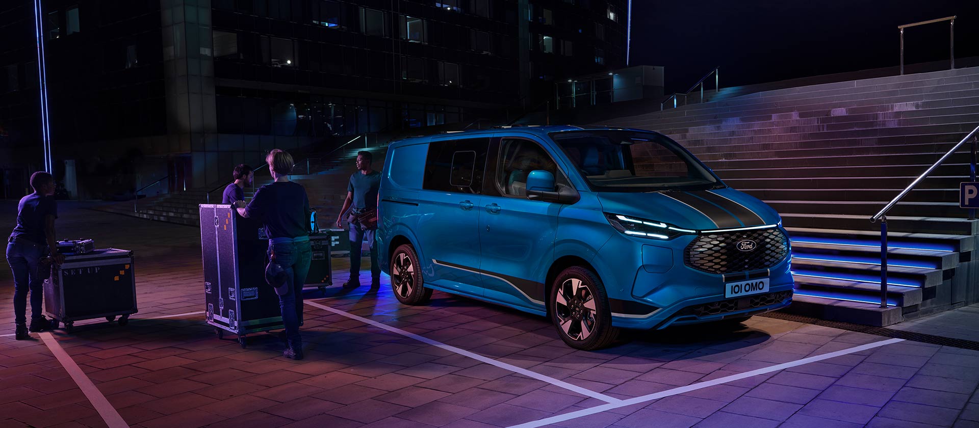Ford E-Transit Custom in Blau. Dreiviertelansicht, parkt vor einer Stiege. Drei Personen beladen das Fahrzeug.