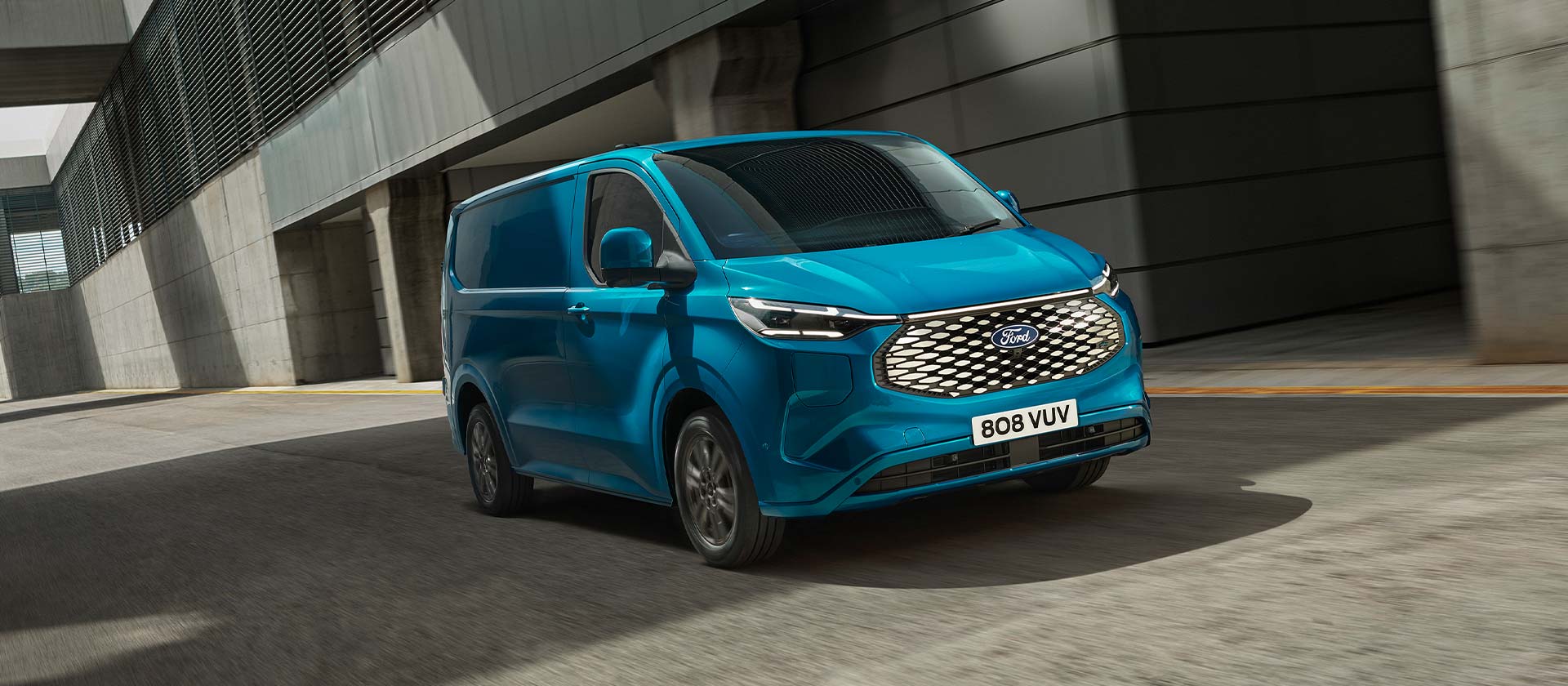 Ford E-Transit Custom in Blau. Dreiviertelansicht, fährt in einem Industriegebiet.