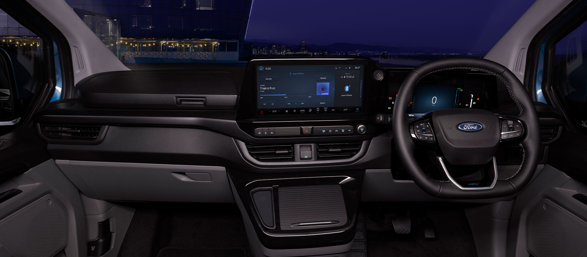 Ford E-Transit Custom Innenraum. Blick durch die Windschutzscheibe bei Nacht mit Ansicht des Lenkrads und Ford SYNC-Touchscreens. 