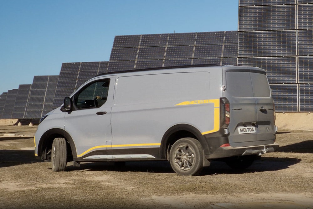 Ford Transit Custom Trail in Grau. Dreiviertelansicht, stehend vor Solarpanelen.