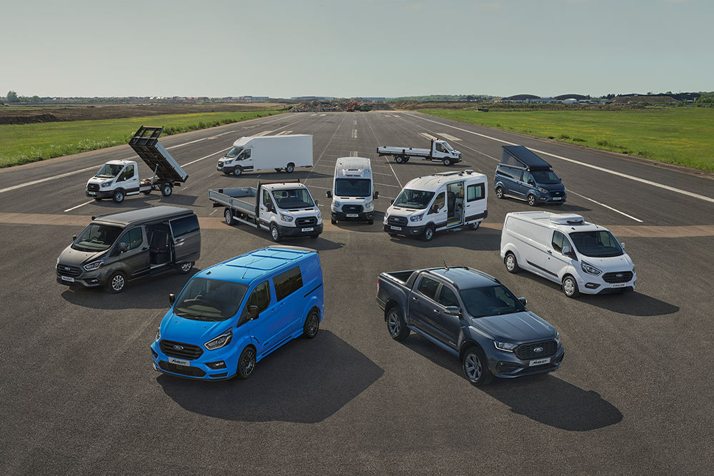 10 Ford Nutzfahrzeuge aus der Vogelperspektive stehen nebeneinander auf einer Fahrbahn.