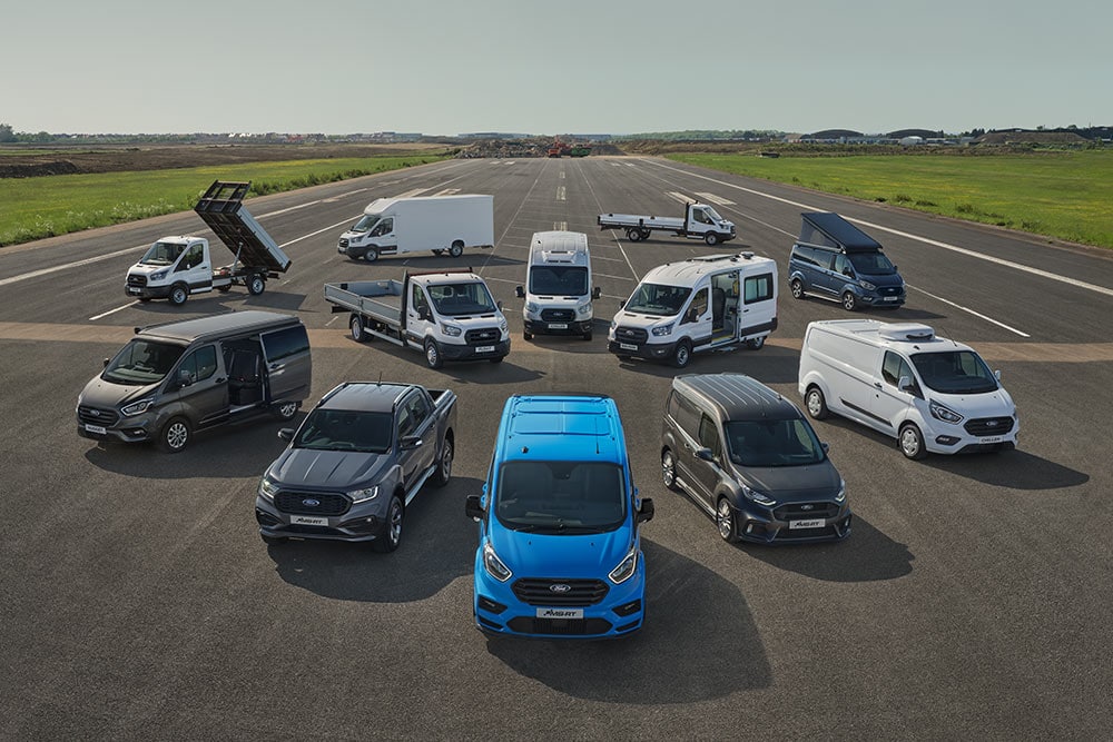 10 Ford Nutzfahrzeuge aus der Vogelperspektive stehen nebeneinander auf einer Fahrbahn.
