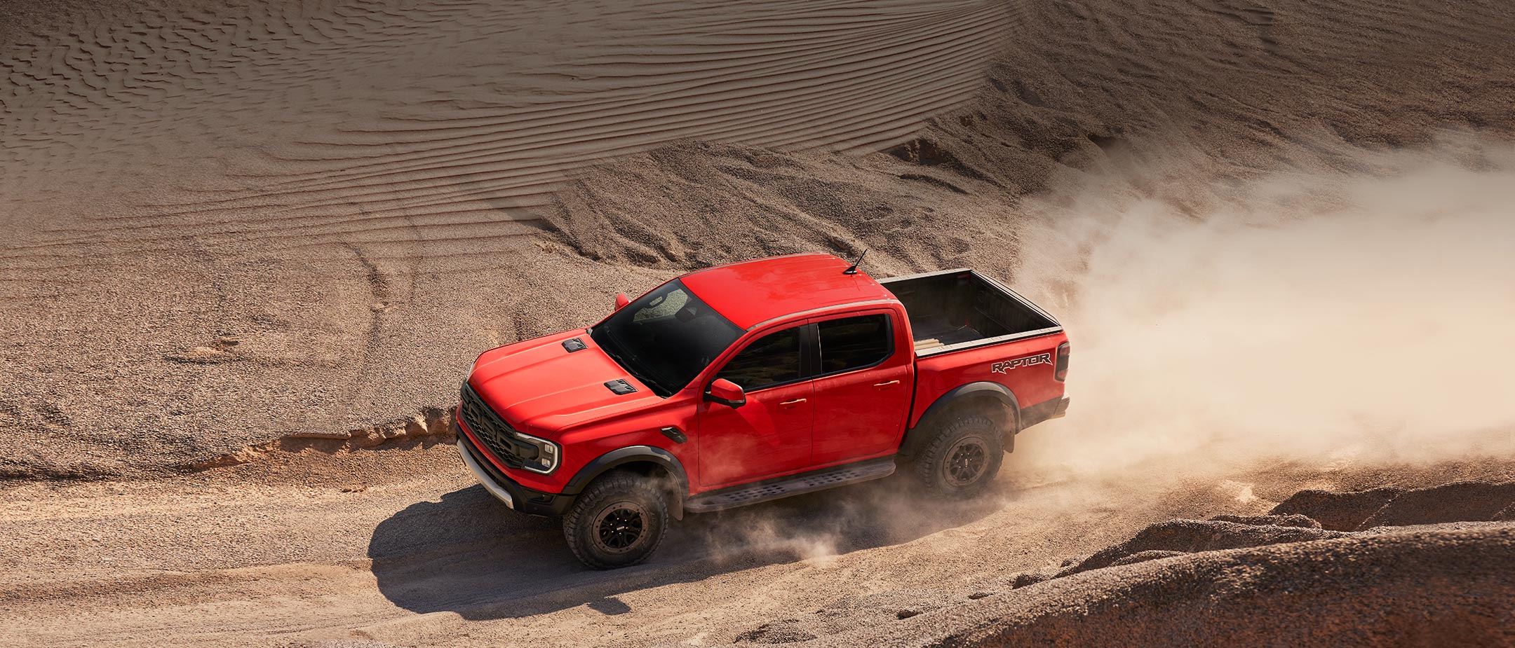 Der Ford Ranger Raptor in Rot. Ansicht von oben, fahrend durch eine Wüste.