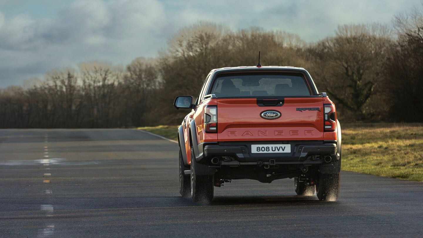 Ford Ranger Raptor in Rot. Heckansicht, fährt auf einer Landstraße.