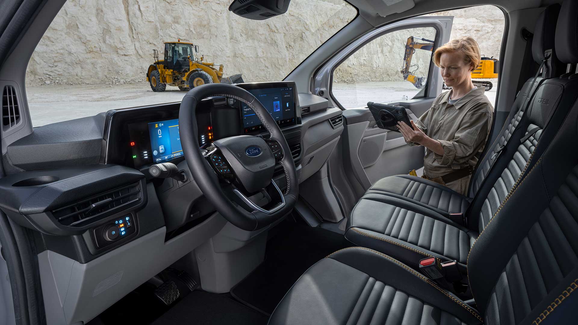 Ford Transit Custom Innenraum. Blick in die Fahrerkabine – eine Person steht bei der geöffneten Beifahrertür und hält ein Tablet in der Hand.