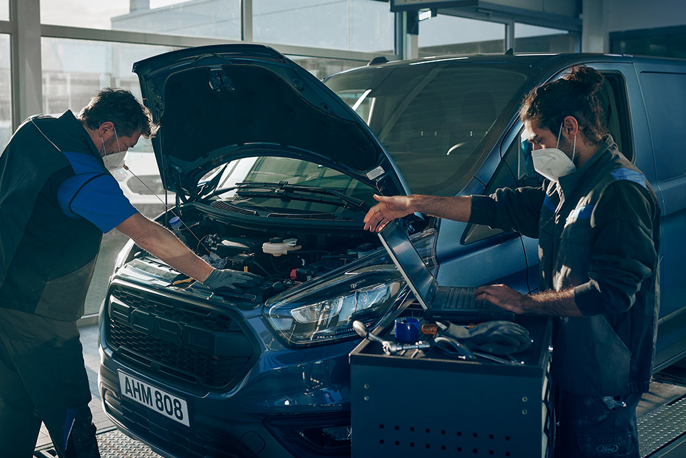Zwei Mechaniker führen Arbeiten an einem Ford Transit Custom in einer Werkstatt durch.