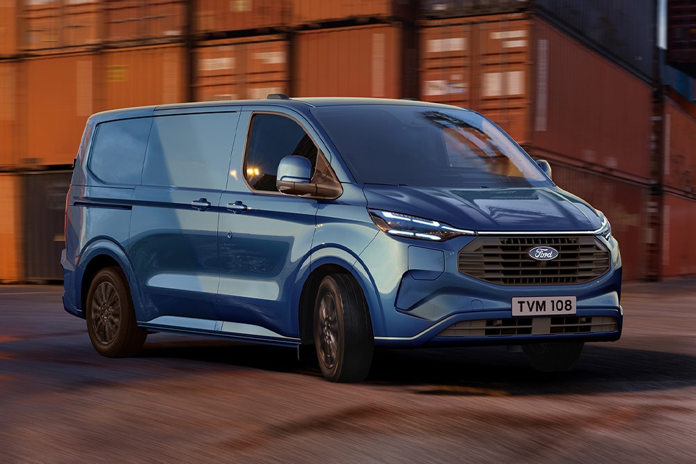 Ford Transit Custom Plug-in-Hybrid in Blau. Dreiviertelansicht, fährt an Containern vorbei.