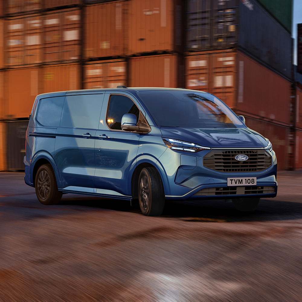 Ford Transit Custom Plug-in-Hybrid in Blau. Dreiviertelansicht, fährt an Containern vorbei.