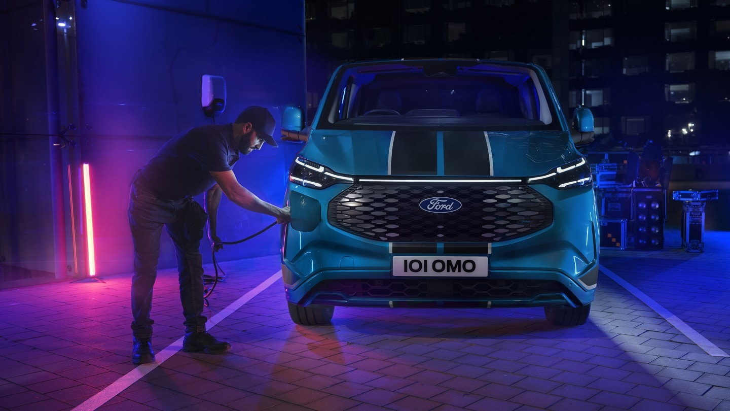 Ford E-Transit Custom in Blau. Frontansicht, Mann schließt Ladekabel an.