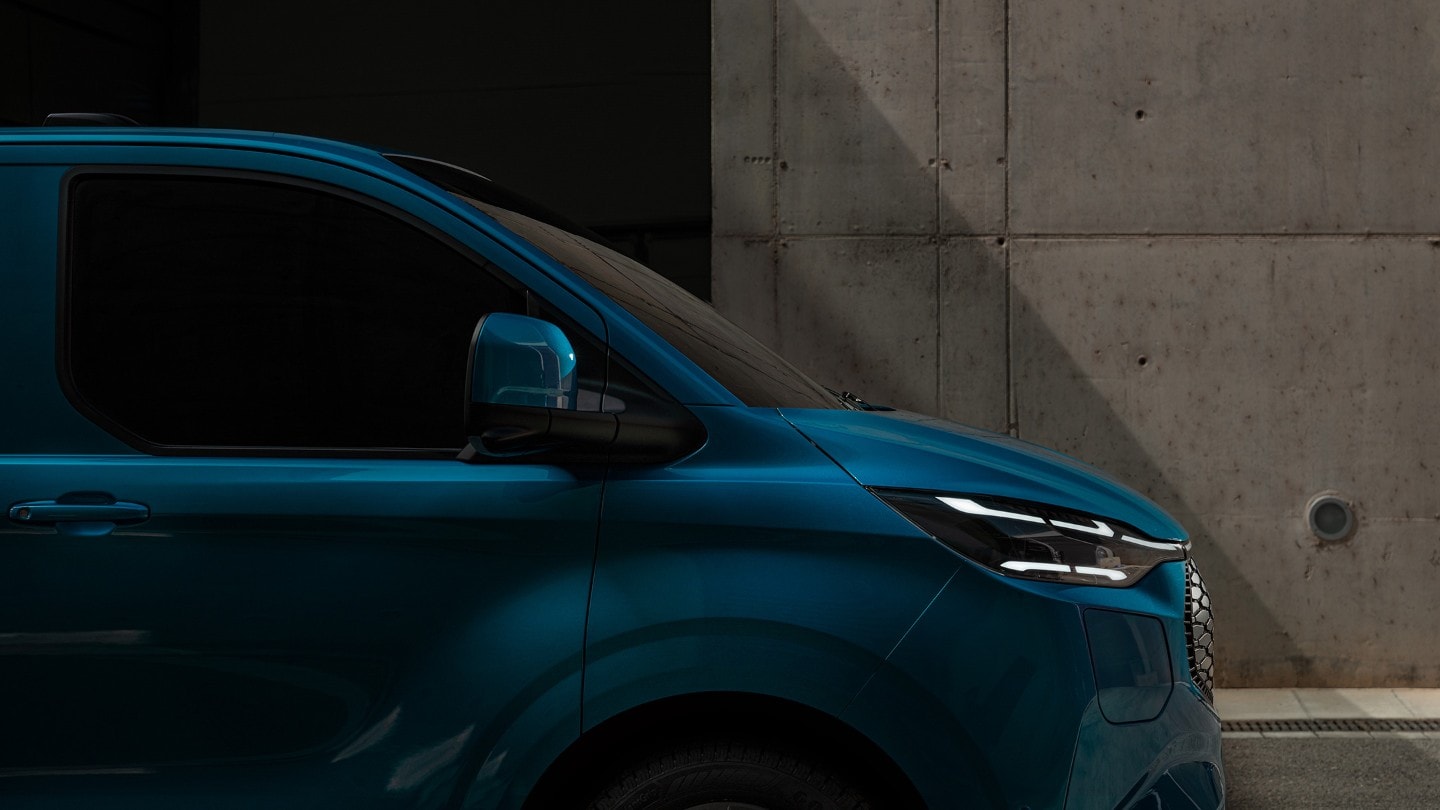 Ford E-Transit Custom in Blau. Seitenansicht, parkt vor einem Gebäude.