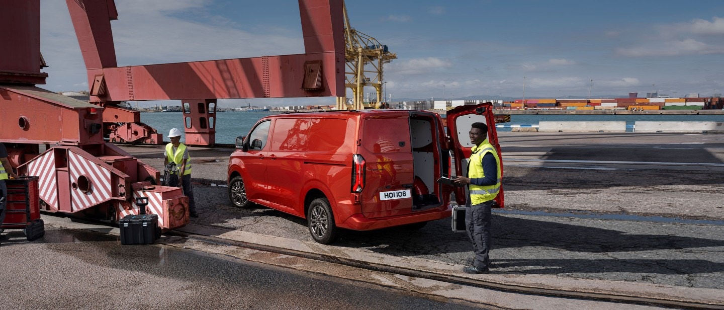 Ford Transit Custom in Rot. Dreiviertelansicht, stehen an einem Hafen mit geöffneter Hecktür.