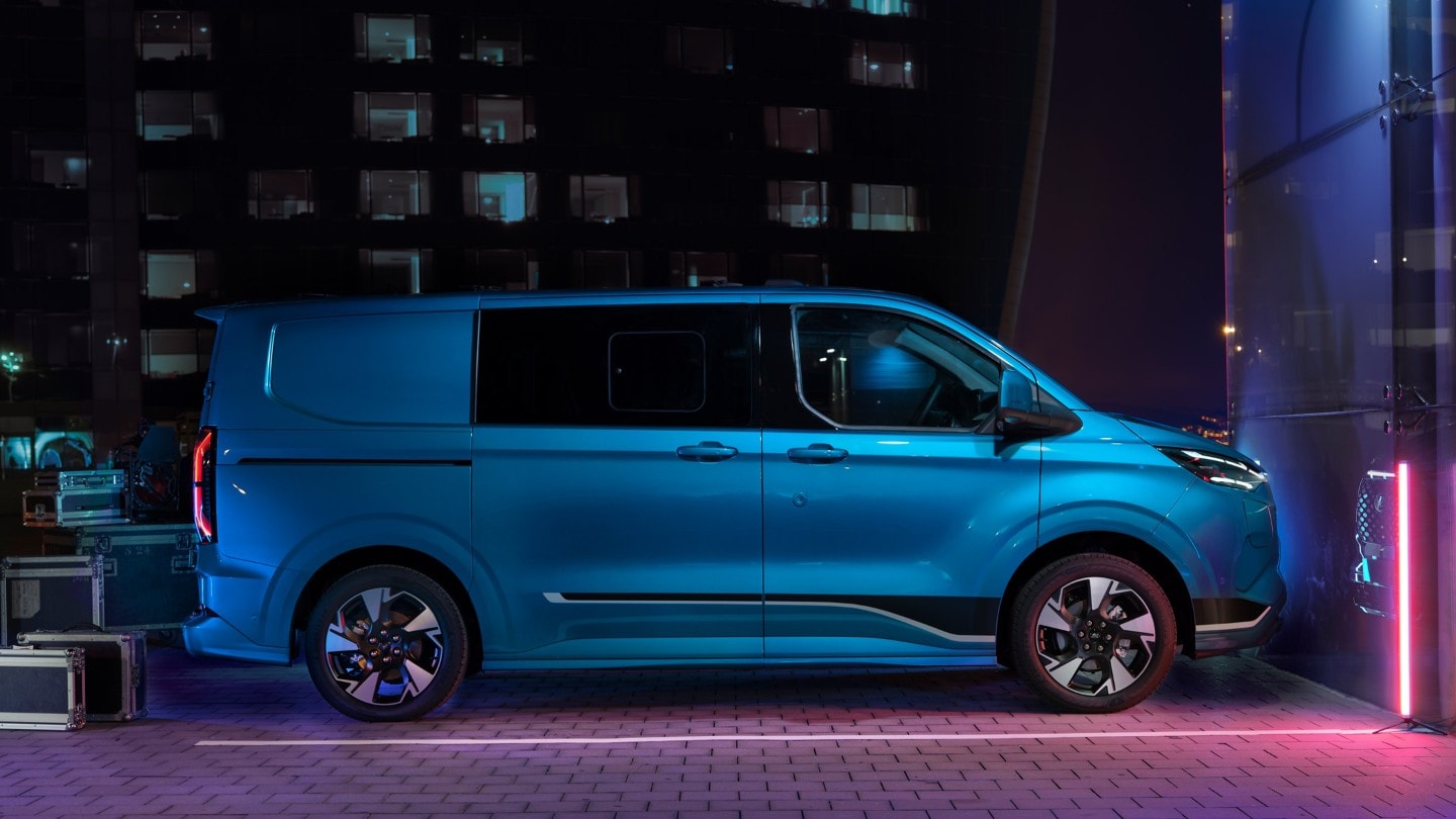 Ford Transit Custom Doppelkabine in Blau. Seitenansicht, parkt vor einem Gebäude bei Nacht.