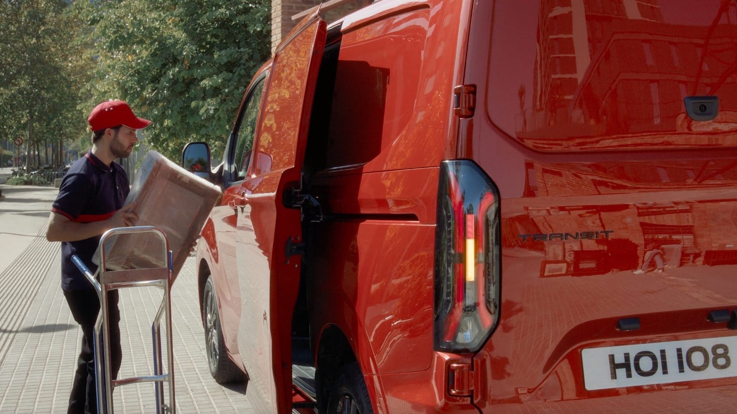 Ford Transit Custom in Rot. Mann beladet den Transporter, Ansicht der elektrischen Schiebetür.