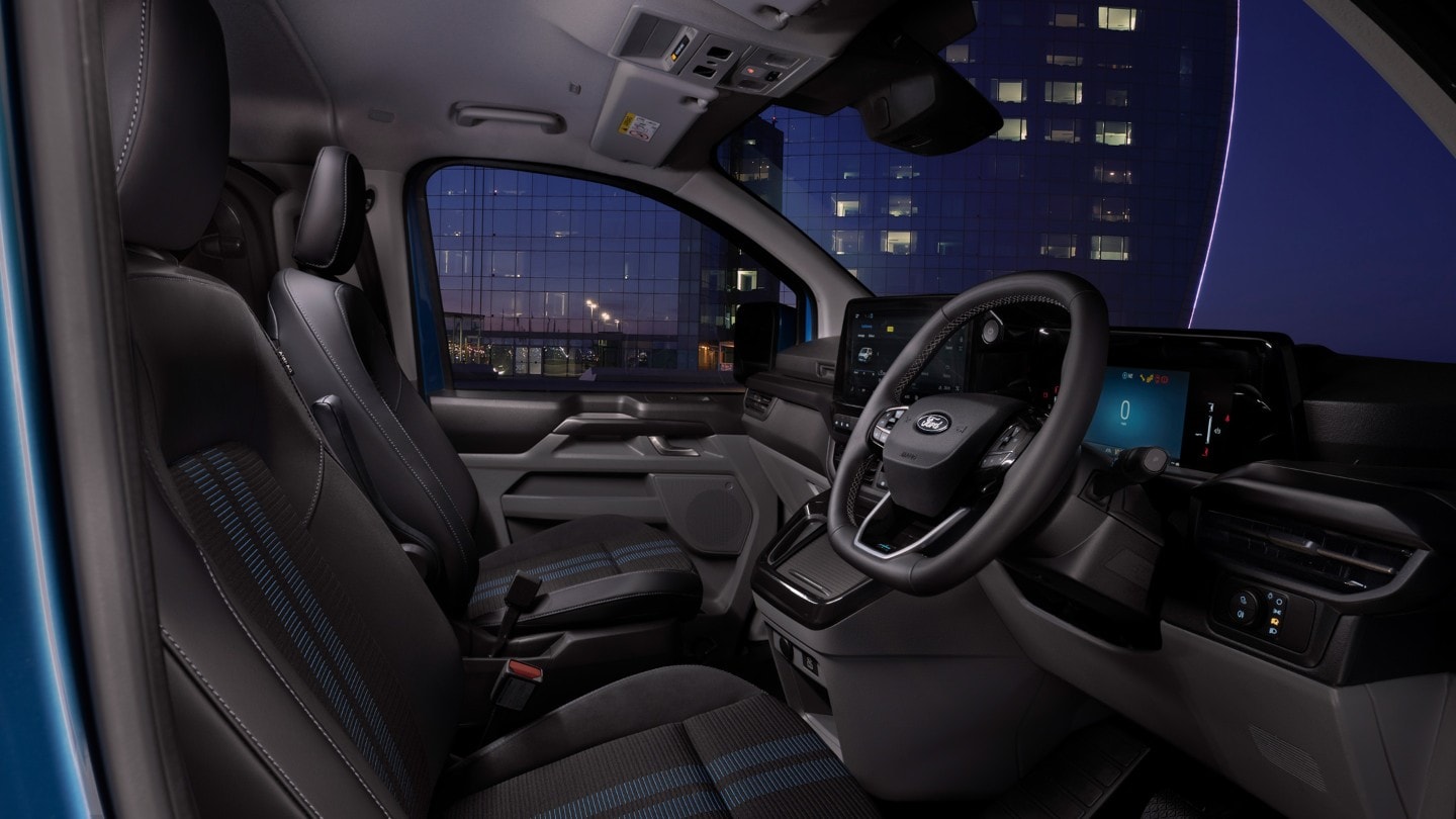 Ford Transit Custom Innenraum. Ansicht auf die vordere Sitzreihe und Instrumententafel bei Nacht.