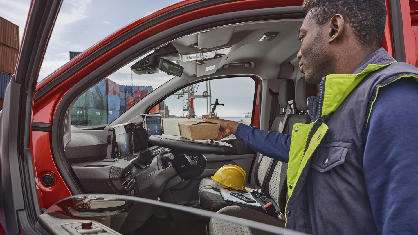 Ford Transit Custom in Rot. Seitliche Ansicht in den Innenraum, Mann stellt sein Essen auf das Lenkrad mit Neigungsverstellung. 