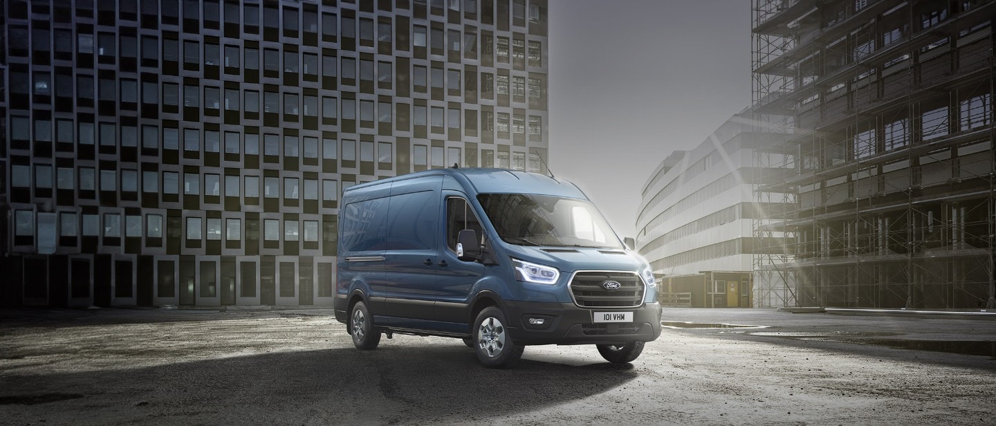 Ford Transit in Blau. Dreiviertelansicht, vor einem Hochhaus bei Sonnenuntergang.