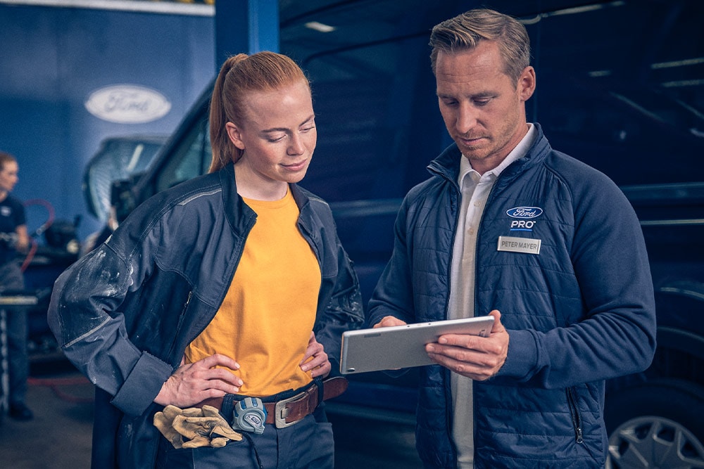 Zwei Ford Mitarbeiter stehen in einem Ford Servicebetrieb und schauen auf ein Tablet.