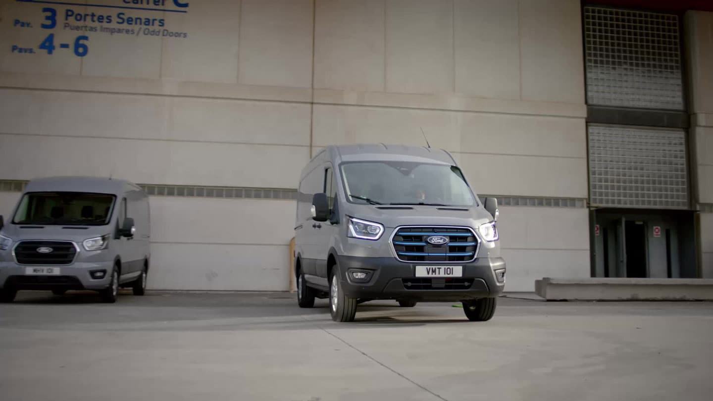 Zwei graue Ford E-Transit vor einem Unternehmensgebäude.