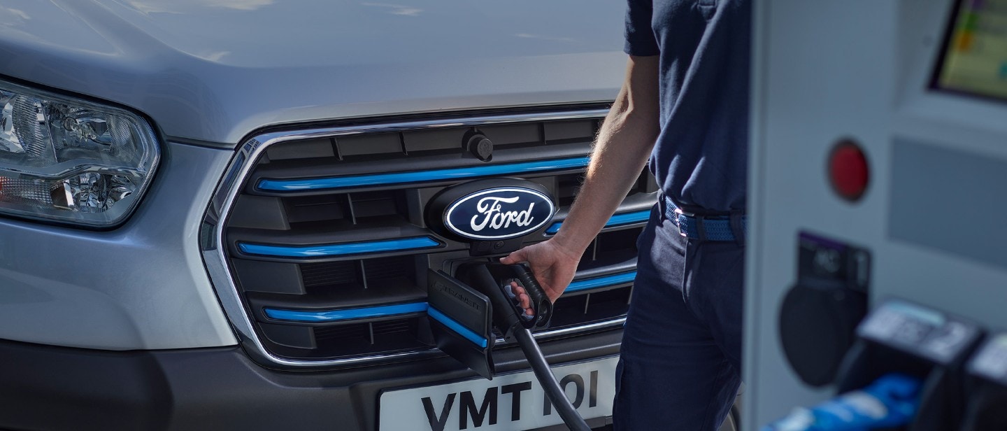 Ford E-Transit in Silber. Detailansicht des Ladeanschluss mit Ladekabel und Ladesäule