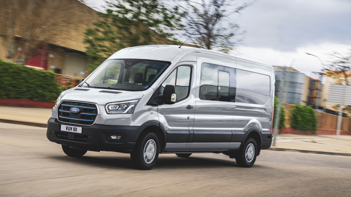 Ford E-Transit Doppelkabine in Silber. Dreiviertelansicht, fahrend auf einer Straße.
