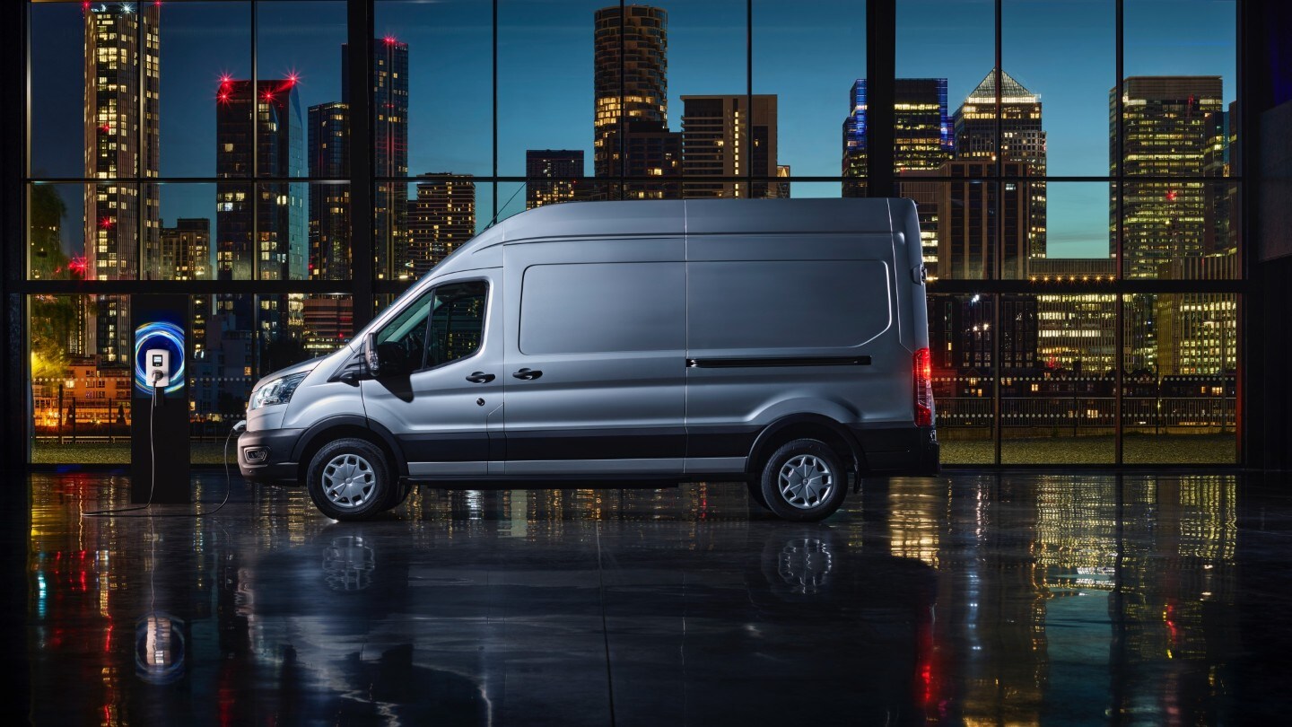 Ford E-Transit Doppelkabine in Blau. Seitenansicht, an einer Ladestation angeschlossen.