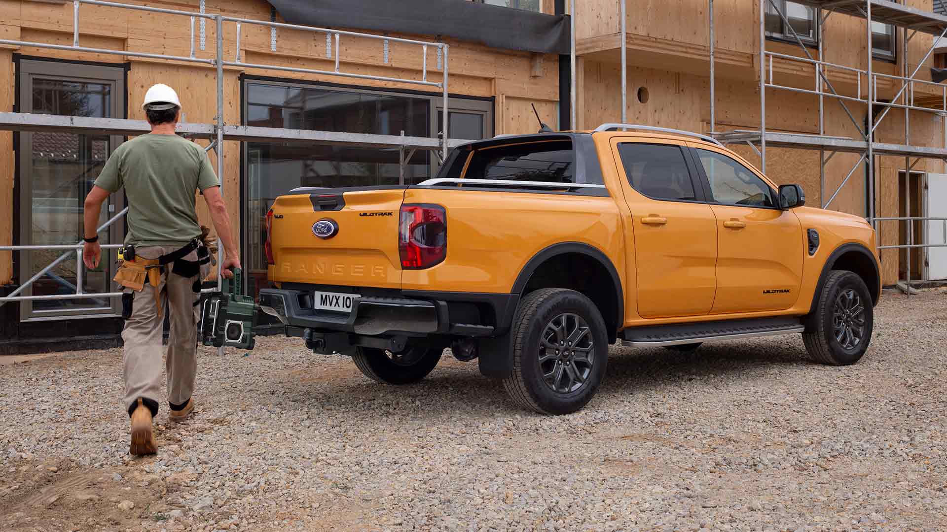 Ford Ranger in Orange. Dreiviertelansicht, geparkt vor einem Haus im Bau mit Gerüst.