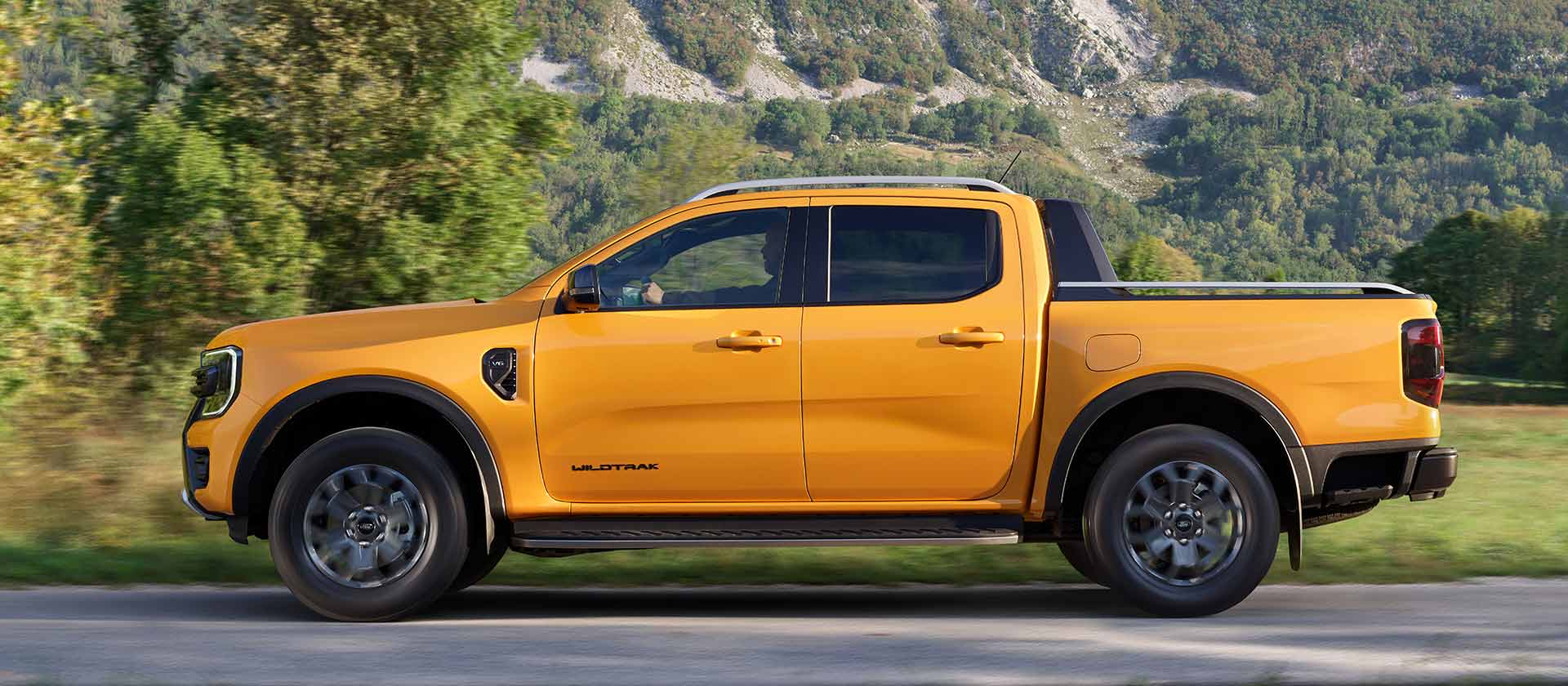 Ford Ranger in Orange. Seitenansicht, fährt durch Gebirgslandschaft.