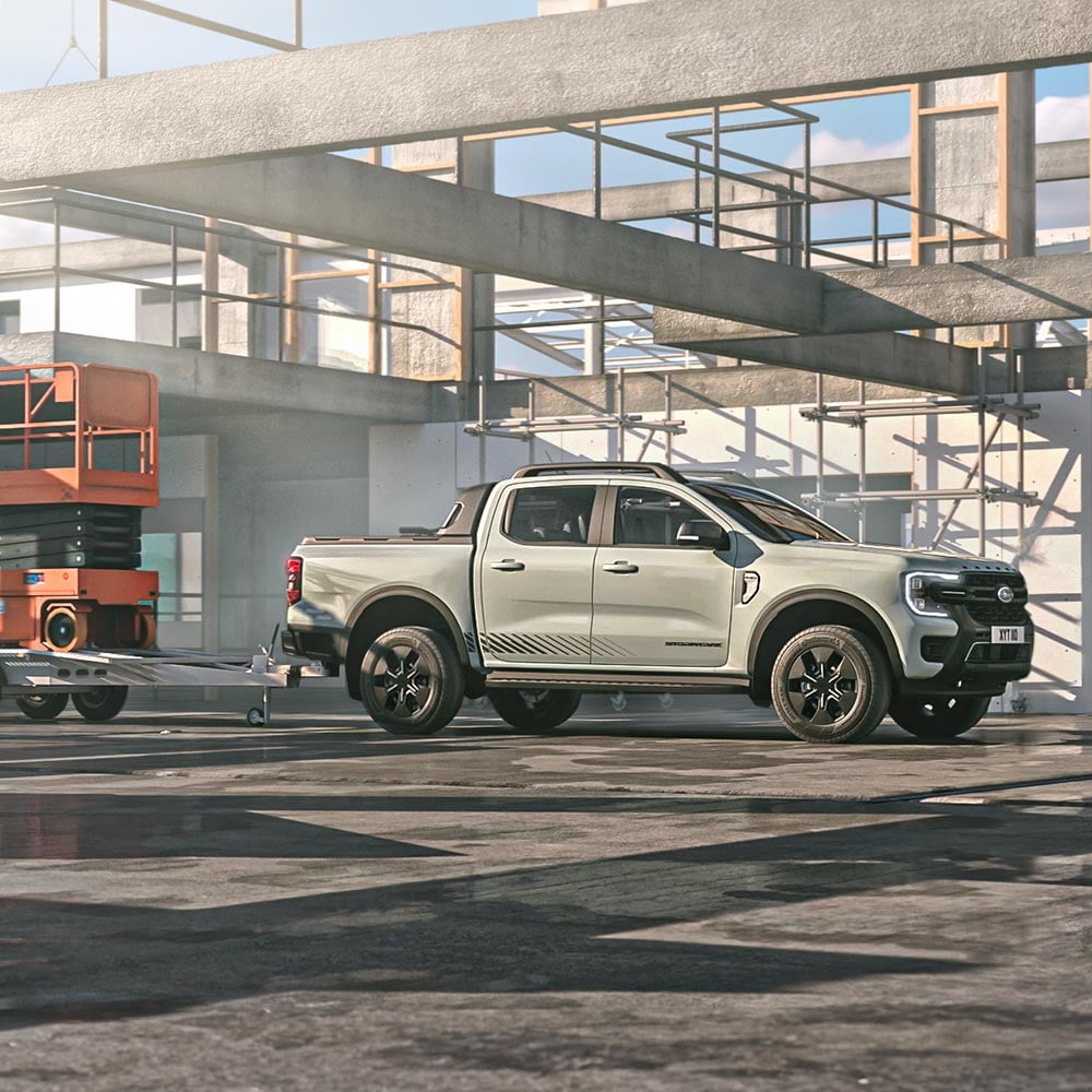 Ford Ranger Plug-in-Hybrid in Grau. Seitenansicht, fahrend durch eine Lagerhalle mit Anhänger.