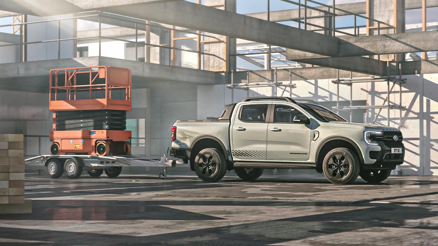 Ford Ranger Plug-in-Hybrid in Grau. Seitenansicht, fahrend durch eine Lagerhalle mit Anhänger.