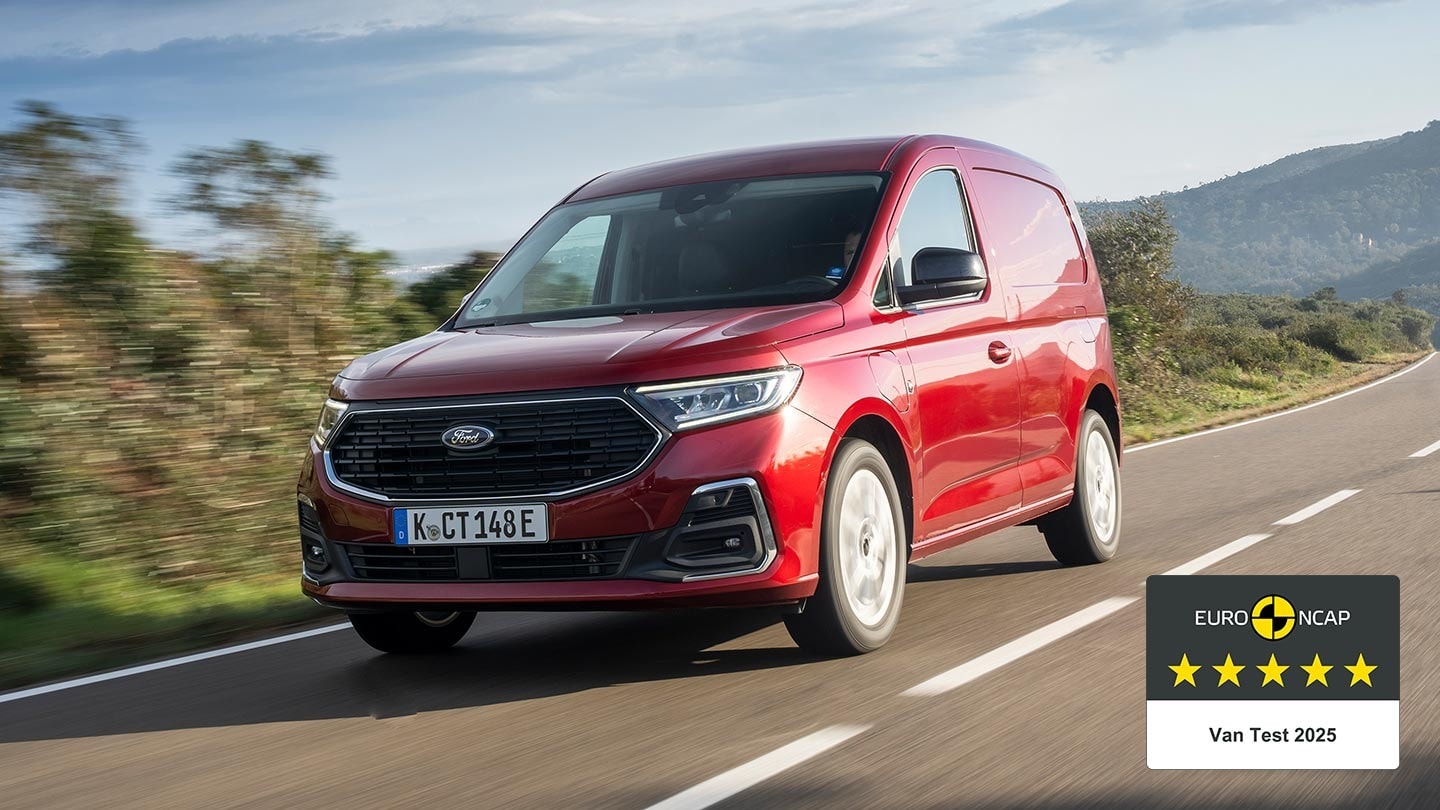 Ford Transit Connect in Rot. Dreiviertelansicht, fährt auf einer Landstraße entlang. Im Hintergrund ein Berg.