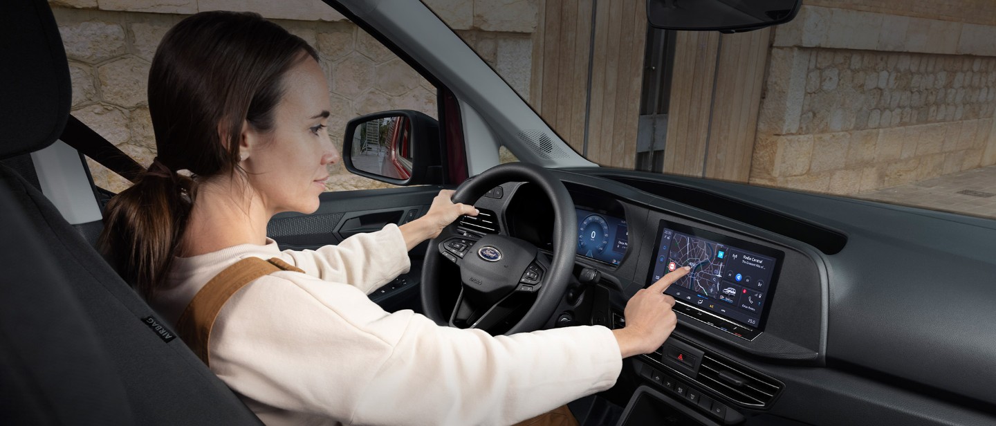 Ford Transit Connect Innenraum. Frau sitzt im Fahrersitz und bedient den Touchscreen.