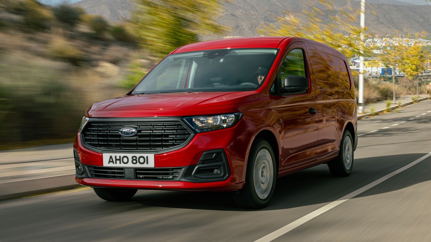 Ford Transit Connect in Rot. Dreiviertelansicht, fahrend auf einer Straße mit Bäumen im Hintergrund.