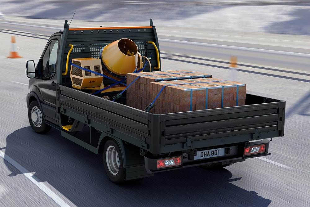 Ford Transit Fahrgestell in Grau mit Ladung auf der Ladefläche während der Fahrt.