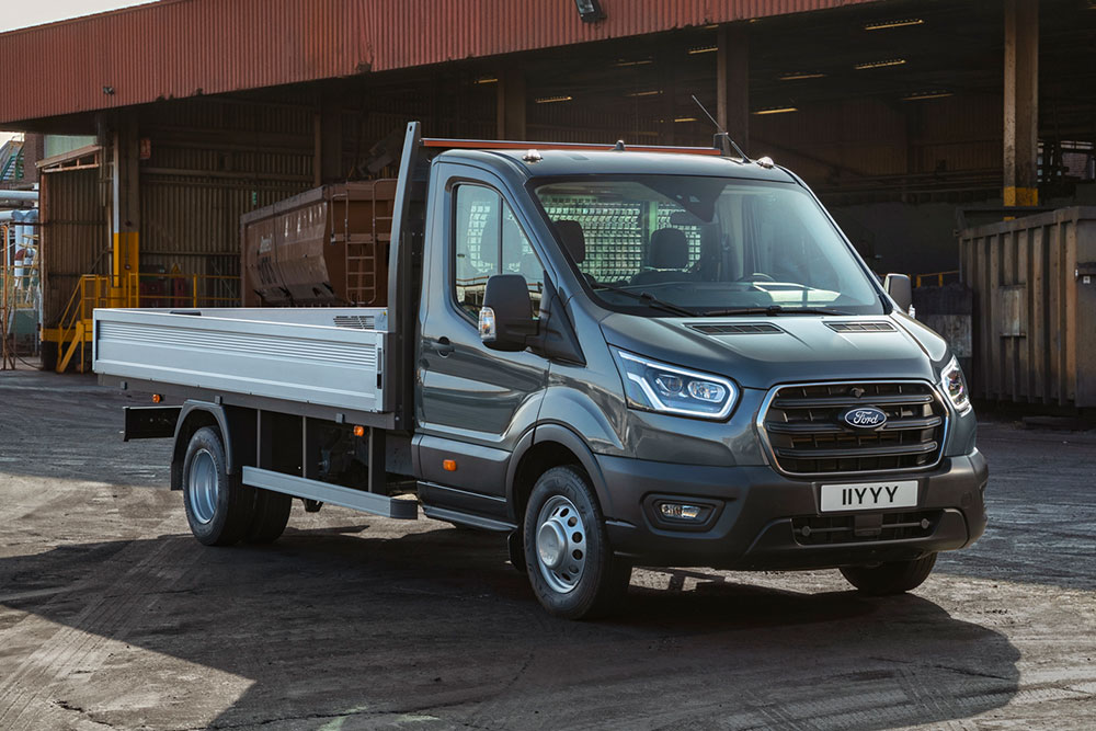 Ford Transit Fahrgestell in Grau. Dreiviertelansicht, geparkt in einem Industriegebiet.