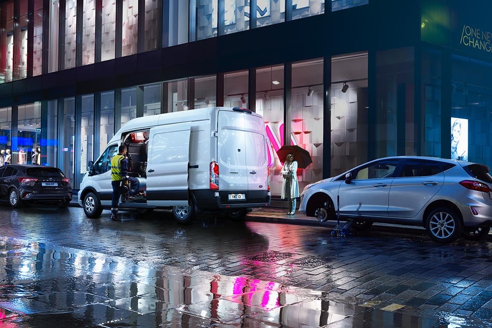 Ford Transit in Weiß. Heckansicht, parkt bei Nacht in einer Stadt.