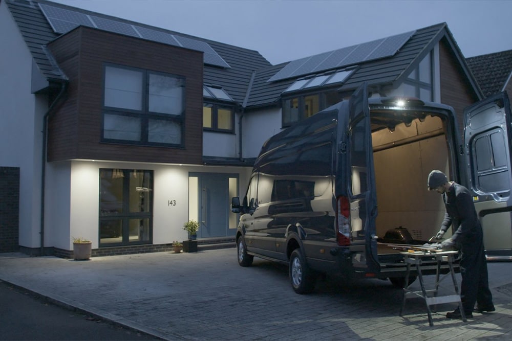 Ford Transit in Blau. Ein Handwerker arbeitet nachts im beleuchteten Heckbereich des Vans.