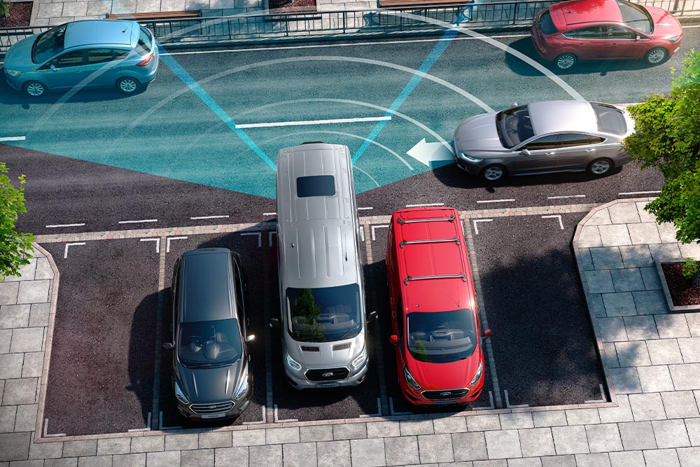 Ford Transit Kastenwagen in Silber beim Rückwärtsfahren mit visualisiertem Erfassungsbereich der Parksensoren.