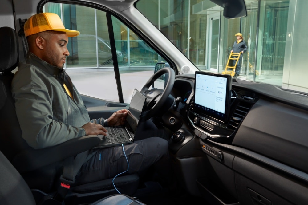 Ford E-Transit Fahrgestell Innenraum. Person sitzt am Steuer und arbeitet an einem Laptop.