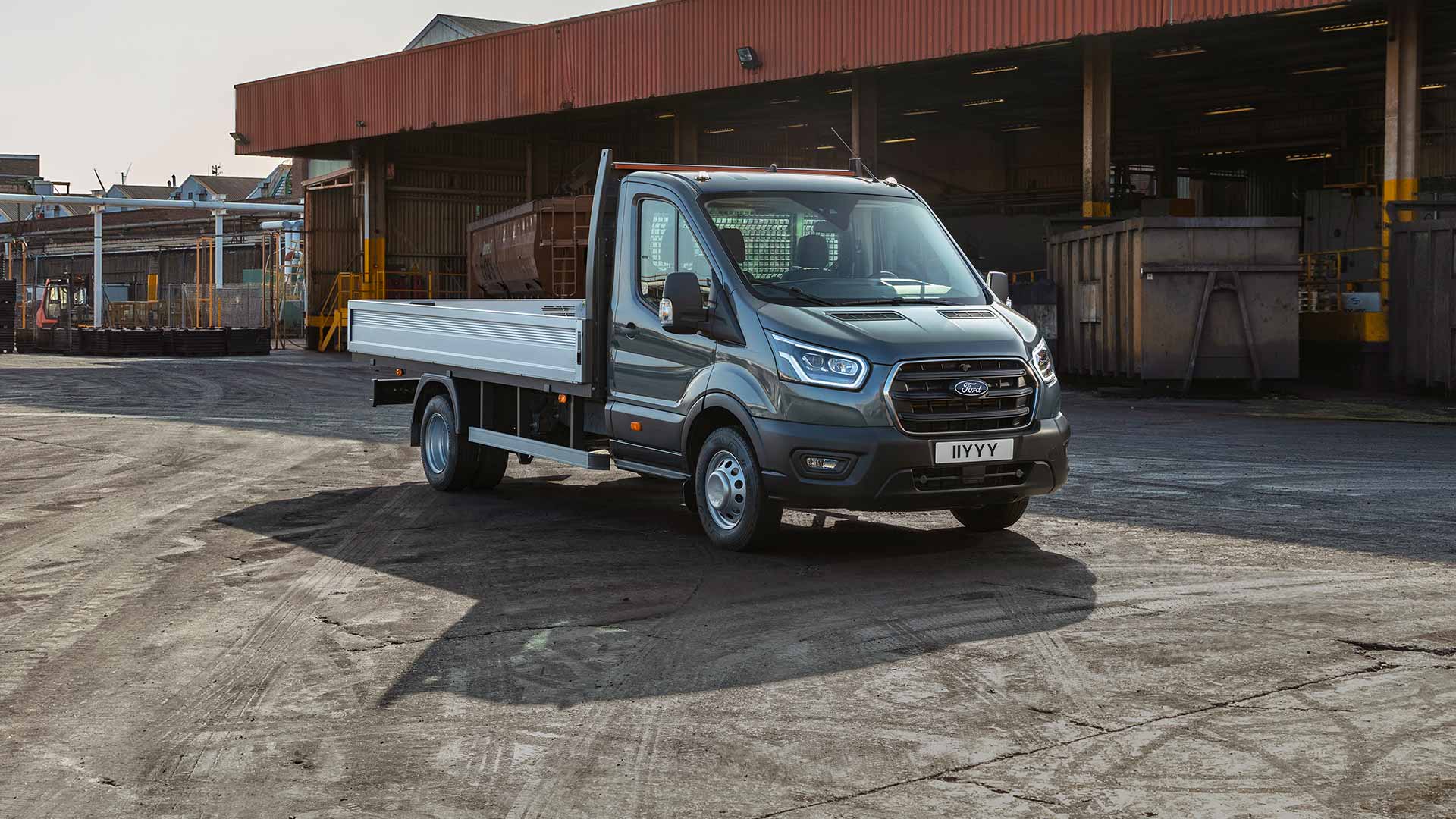 Ford Transit Fahrgestell in Grau. Dreiviertelansicht, parkt auf einem Industriegelände.