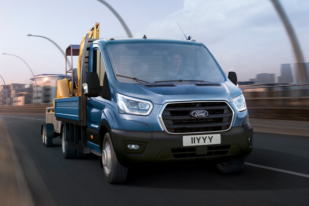 Ford Transit Pritschenwagen mit Einzelkabine in Blau. Frontansicht, fährt über eine Brücke.