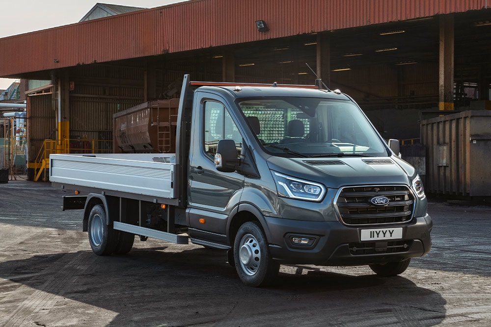 Ford Transit Fahrgestell in Grau. Dreiviertelansicht, parkt auf einem Industriegelände.