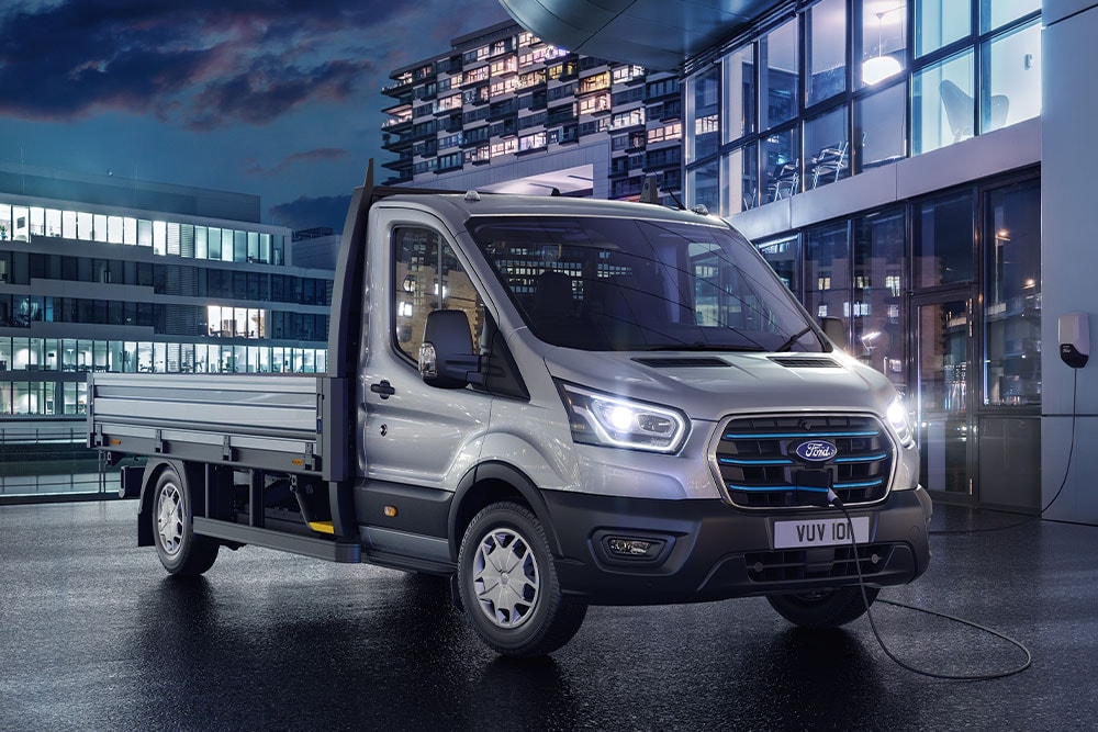 Ford E-Transit Fahrgestell in Silber. Dreiviertelansicht, stehend auf einem Parkplatz bei Nacht.