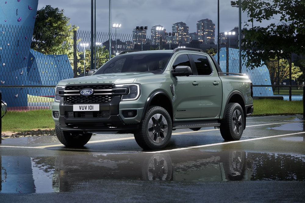 Ford Ranger Plug-in-Hybrid in Grau. Dreiviertelansicht, auf einem nassen Parkplatz vor einer Boulder-Anlage. 