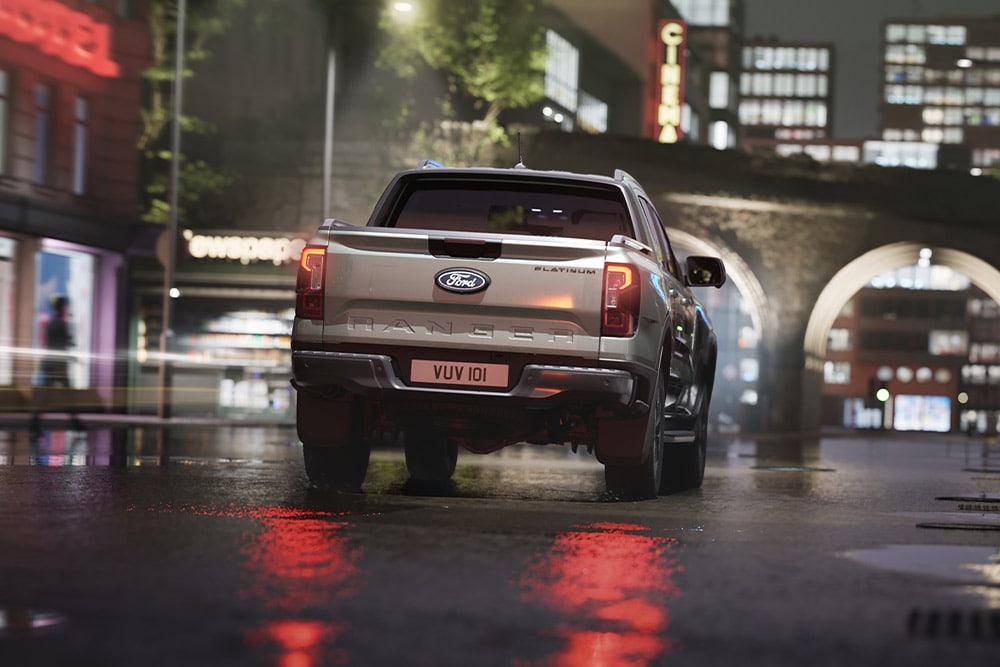 Ford Ranger in Silber. Heckansicht, fährt bei Nacht durch eine beleuchtete Innenstadt.